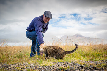 ein Mann streichelt eine schmusebedürftige Katze vor einem landschaftlich sehr schönen Hintergrund
