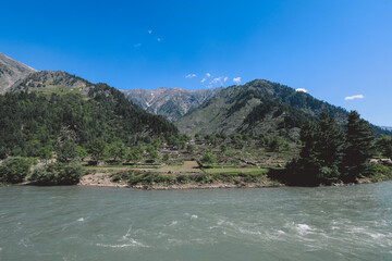 Naklejka na ściany i meble Fast River and Green Mountain Forest under the Blue Sky in Gilgit Baltistan Highlands, Pakistan