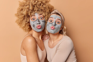 Funny two female models keep lips rounded make funny grimace apply nourishing clay masks on face...