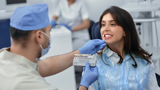 Male dentist choosing enamel samples shade color tone veneer teeth prosthesis whitening to woman 