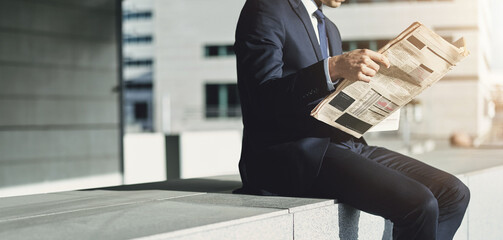Businessman sitting outside an office building reading a financial newspaper