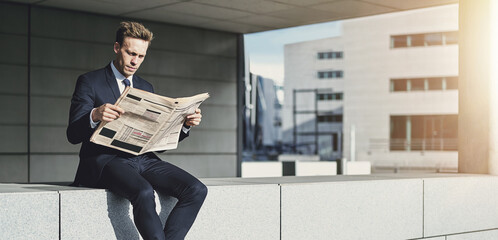 Focused young businessman sitting outside reading a financial newspaper
