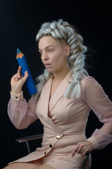 Obraz premium beautiful young surprised blonde woman holding big blue pencil and looking aside while sitting on black background