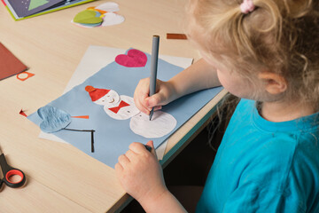 preschooler girl in a blue t-shirt makes an applique while sitting at the table, paper snowman