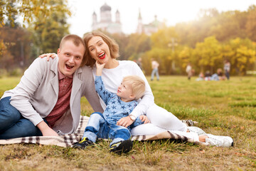Naklejka na ściany i meble Happy family with child having fun in autumn park sitting on a plaid.