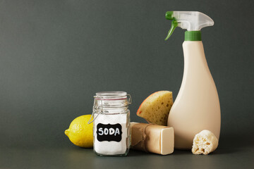 spray bottle, soap, luffa, soda jar, lemon, wooden brush and sponge on hb dark green background...