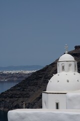 View of a beautiful whitewashed and traditional Orthodox Church, the volcanic landscape and the village of Oia in the background  in Santorini Greece