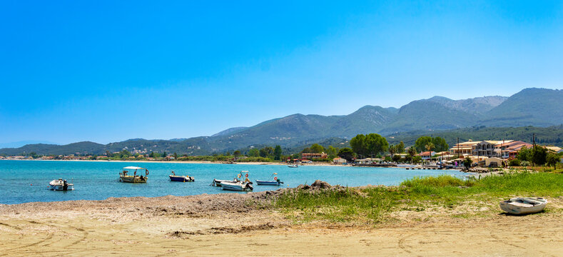 Panorama of Roda tourist town on Corfu island, Greece. Picturesque fishing village on seashore with colorful houses, boats in bay, turquoise water and mountains. Popular tourist destination