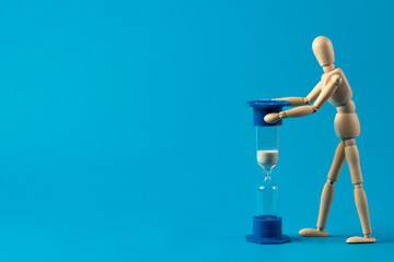 Wooden man and hourglass   on a blue background. Time management concept. Copy space.