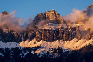 Bergkette von Wolken umgeben wird von der Sonne angeschienen. Ein nebulöses, eindrückliches Bild.