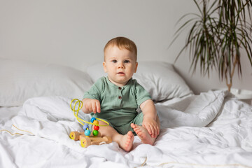 cute baby in a green cotton bodysuit plays with wooden educational toys while sitting in bed. products for children, early development, nursery kindergarten. space for text. High quality photo