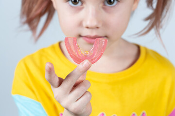 Cute little girl with blond hair is holding a pink dental myofunctional trainer