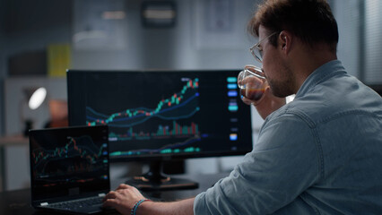 Side view of financial expert analyze graphs on computer and drink coffee working late in office. 