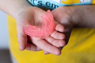 Cute girl with blond hair is holding a pink dental myofunctional trainer