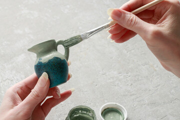 A woman is decorating with new paint an old tiny vase. - obrazy, fototapety, plakaty