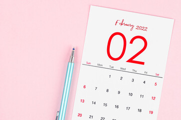 February 2022 calendar with pen on pink background.