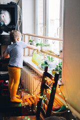 Caucasian boy watering from a yellow watering can home plants on the windowsill