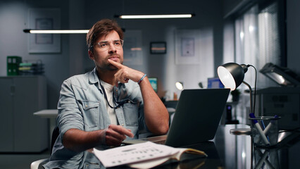 Pensive male manager sitting at desk and thinking in modern open space office. 