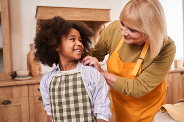 Caucasian mother and multiracial child looking at each other while standing at the kitchen