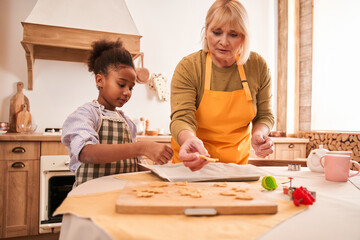 Grandmother enjoying weekend with small girl child while baking biscuits pastries at the kitchen