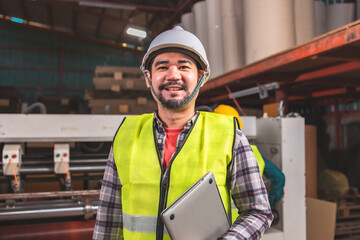 Engineer asian worker wearing safety helmet and vest holding clipboard and take note or tablet in the automotive part warehouse.Products and corrugated cardboard..