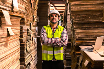 Engineer man wearing safety helmet and vest holding clipboard and take note on the paper in the automotive part warehouse.Products and corrugated cardboard. 