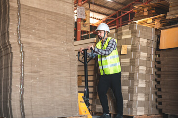 Engineer  wearing safety helmet and vest holding clipboard and take note on the paper in the automotive part warehouse.Products and corrugated cardboard. 