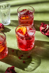 Cocktail with pomegranate juice and ice in a glass on a light green background