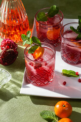 Cocktail with pomegranate juice and ice in a glass on a light green background