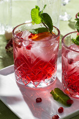 Cocktail with pomegranate juice and ice in a glass on a light green background