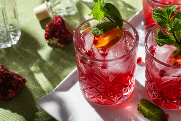 Cocktail with pomegranate juice and ice in a glass on a light green background