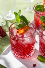 Cocktail with pomegranate juice and ice in a glass on a light green background