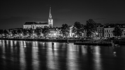 Fototapeta premium An illuminated church towers from the skyline along a river in the city of Kampen in the Netherlands