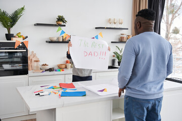 Boy showing placard to his daddy while congratulating him with Fathers Day at the kitchen