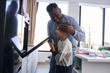 Happy multiracial man bonding to his curious caucasian son while he looking into the oven