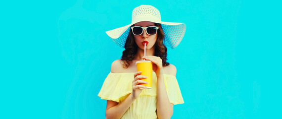Portrait of beautiful young woman drinking a fresh juice wearing a summer hat on blue background - obrazy, fototapety, plakaty