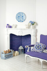 Living room with a bright blue sofa very peri color 2022. Fireplace, candles and flowers, cozy home in trendy colors