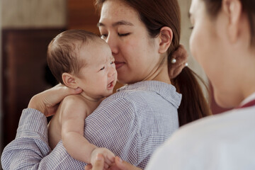 A newborn baby is crying on her mother's shoulder for fear of the doctor coming to check because she is sick in the hospital.