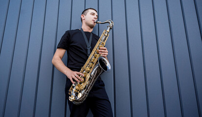 Young street musician playing saxophone near the big blue wall