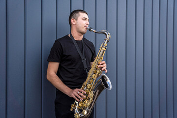 Young street musician playing saxophone near the big blue wall