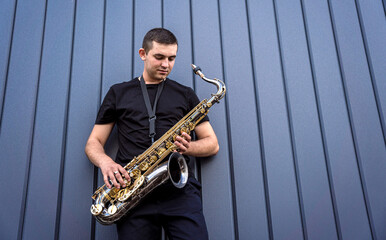 Fototapeta premium Young street musician playing saxophone near the big blue wall