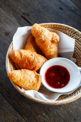 French croissant with jam in wicker basket on wooden table.