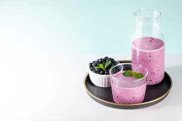 Glass and bottle of blueberries smoothie, blueberries bowl on round plate on white-turquoise.