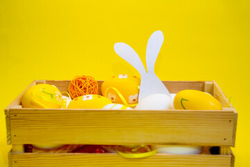 Colorful Easter eggs in a wicker basket and a wooden box on a yellow, green background. Space for...