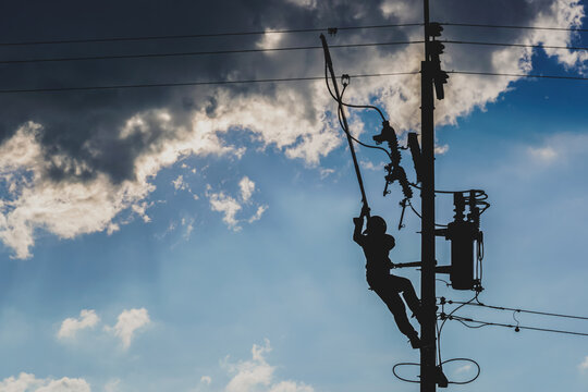 The silhouette of power lineman replacing a transformer and hotline clamp, bail  clamp. Using clamp stick grip all type, wearing personal protective equipmen,