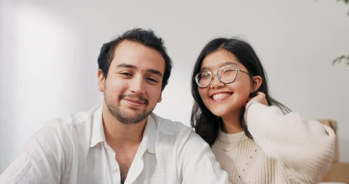 Lovers are sitting on floor in newly bought apartment elegantly dressed man is holding tablet couple is chatting with parents friends over internet waving to camera bragging about moving into flat