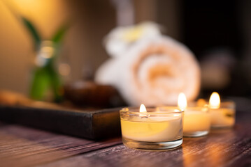 Close up aroma candle, clean rolled towel, stone, flower on the tray over wooden background. Facial spa set, wellness well-being lifestyle concept - obrazy, fototapety, plakaty