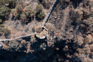 Aerial view of ruins of ancient fortress wall and burnt trees after wildfires, Peloponnese, Greece