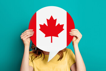girl holds blank white speech bubble with canadian flag isolated on blue background. Invitation to...