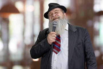 Old elegant man talking in microphone on abstract bokeh background.